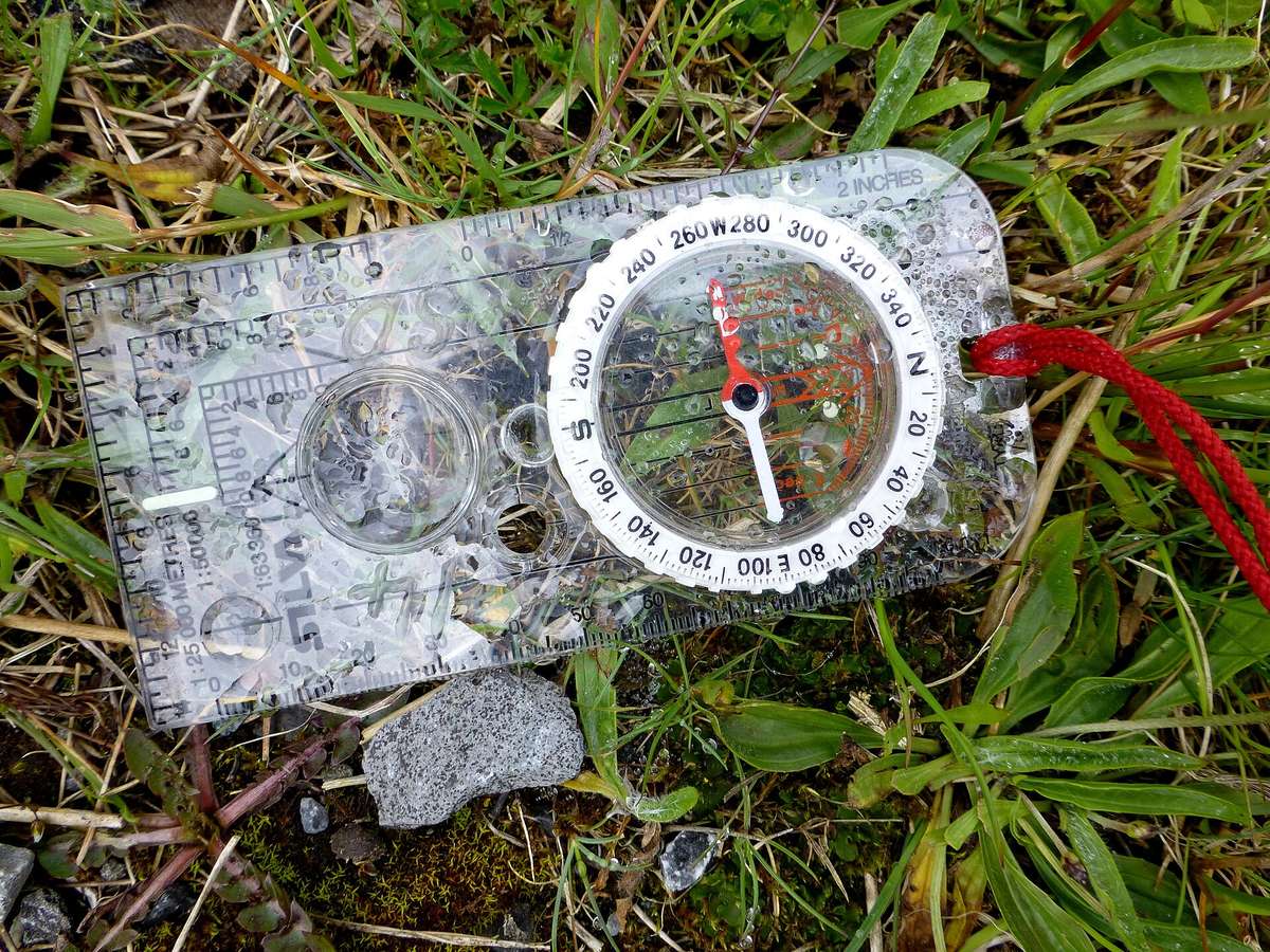 A baseplate compass resting on a folded topographic map in the grass.